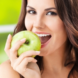 Portrait of young woman eating green apple, outdoors