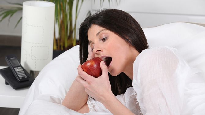 Девушка в постели ест красное яблоко